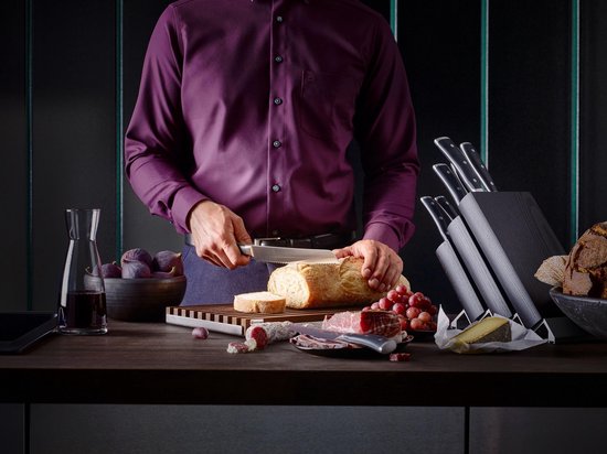 Een man snijdt een brood met een Wüsthof mes in een keuken setting met een messenset.