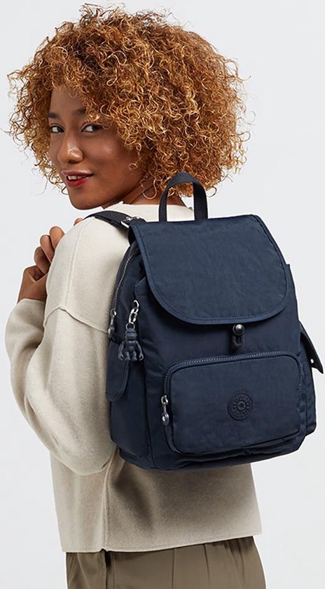Vrouw met krullend haar draagt een donkerblauwe Kipling rugzak met klep en ritsvak op haar schouder.