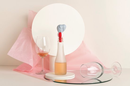 Een grijze olifantjes-wijnstopper op een fles, in een stillevensetting met wijnglazen.