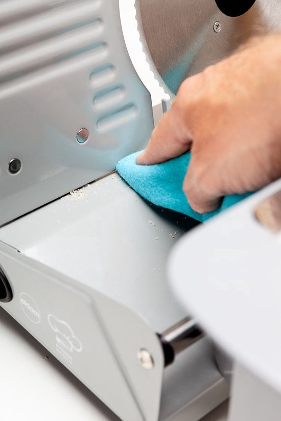 Hand met een blauwe doek maakt de zilverkleurige snijmachine schoon.