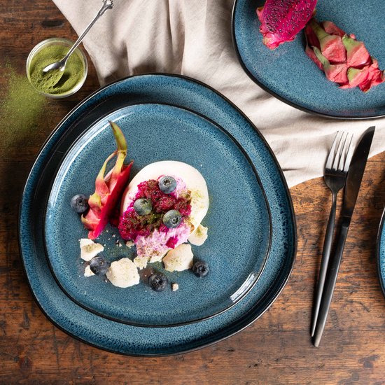Een organische blauwe schaal met een dessert, drakenfruit en bosbessen, met een kopje matcha poeder.