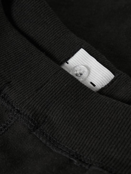 Detail van de binnenkant van de tailleband van een zwarte joggingbroek met knopen voor verstelling.
