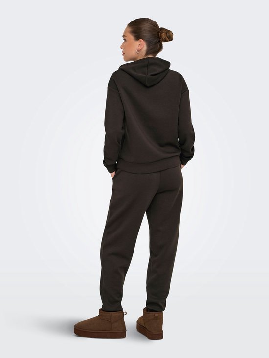 Model van achteren in een donkerbruine hoodie en bijpassende broek, met de handen in de zakken.