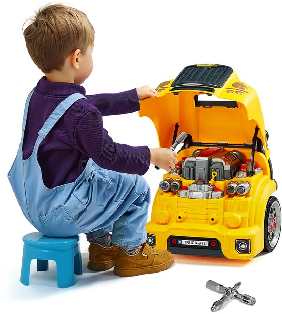Een jongen in overall repareert een gele speelgoed vrachtwagen met een gereedschap.