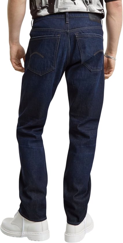 Donkerblauwe G-Star jeans, gedragen door een man, zittend. Zicht op de achterkant.