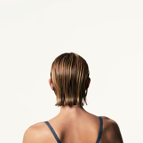 Achterkant van een vrouw met kort, nat blond haar met highlights, een grijze top.