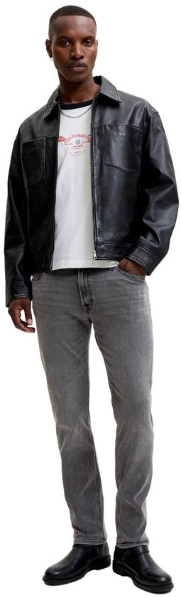 Model in een zwarte imitatielederen jas, wit T-shirt en grijze regular fit jeans.