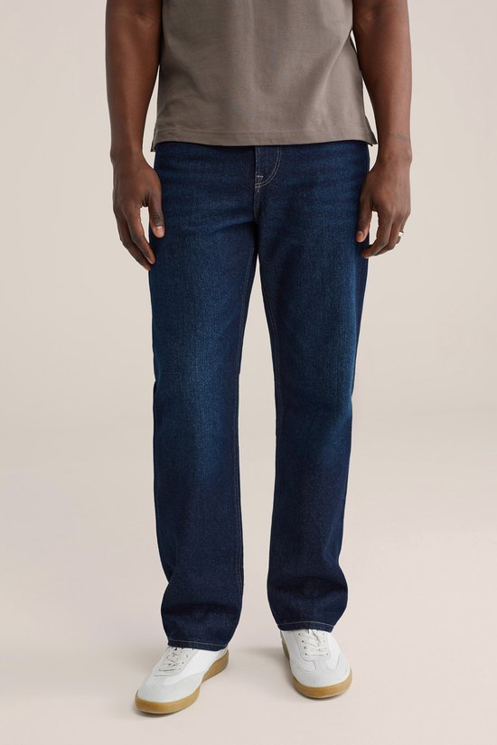 Man in donkerblauwe jeans en witte sneakers, detail van de voorkant.