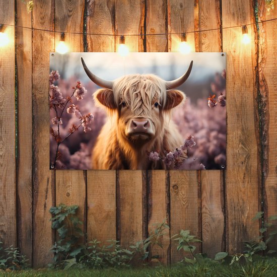 Een bruine Schotse hooglander met lange, golvende vacht staat in een veld met roze bloesems.