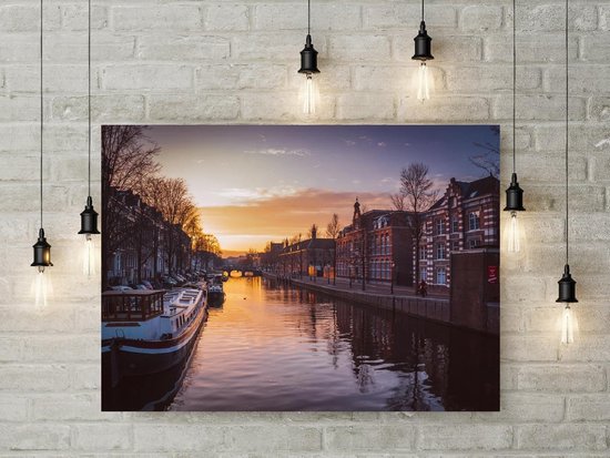 Un bateau est amarré le long d'un canal bordé de maisons et d'arbres au coucher du soleil. Le ciel est orange et violet.