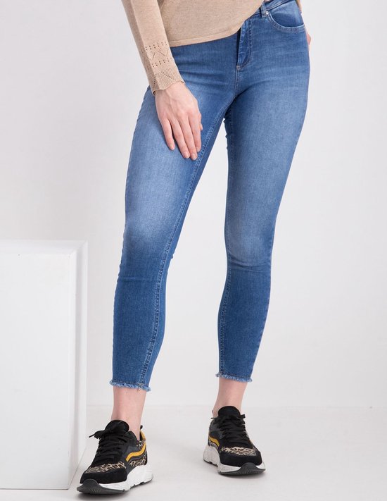 Een model draagt een nauwsluitende jeans met een lichte denim wassing en rafelige zoom, gecombineerd met sneakers.