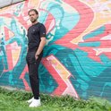 Man in zwarte joggingbroek en zwart T-shirt, staand voor een muurschildering.