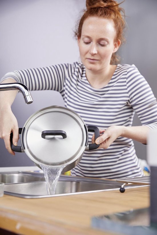 Vrouw met rood haar die water uit een roestvrijstalen pan met deksel afgiet in een gootsteen.