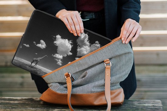 Housse pour ordinateur portable noire avec imprimé d'une girafe dans un champ sous un ciel nuageux. La housse est glissée dans un sac rayé.