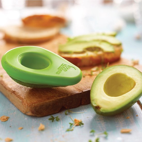 Een groene avocado bewaardoos op een houten plank, met een halve avocado ernaast. Achtergrond met toast.