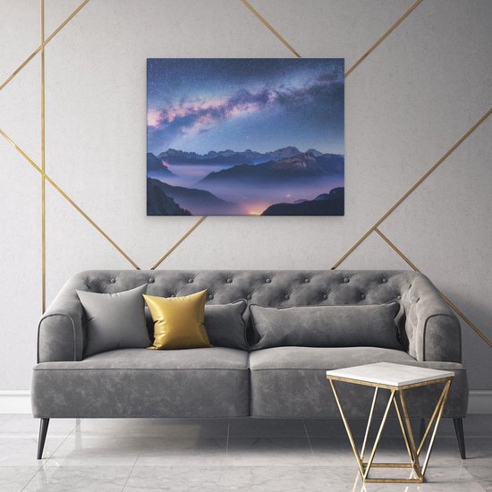 Toile au-dessus d'un canapé gris représentant la Voie lactée, des montagnes et une vallée brumeuse.