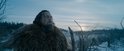 Leonardo DiCaprio met baard en een dikke bontjas, kijkend omhoog in een besneeuwd, mistig landschap.