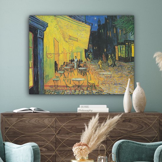 Een woonkamer met een kunstwerk van een caféterras 's avonds met een gele muur.