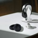 Twee zwarte fluwelen oorkussens op een witte tafel met een witte koptelefoon op een standaard.