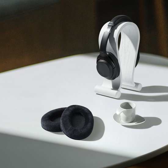 Twee zwarte fluwelen oorkussens op een witte tafel met een witte koptelefoon op een standaard.