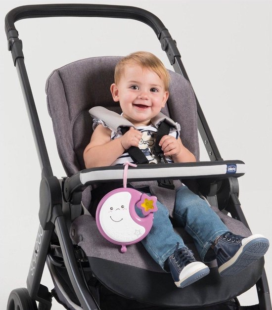 Baby ligt in een wieg met een roze muziekmobiel met maan, sterren en teddybeer.