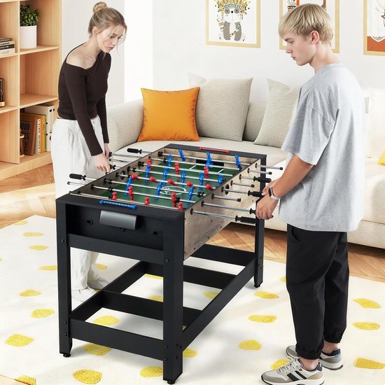 Een stel speelt op de tafelvoetbaltafel in een woonkamer.