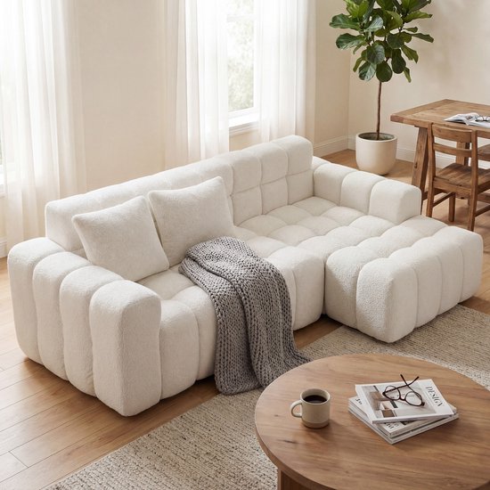 Modulaire witte hoekbank met teddy stof, een grijze plaid en witte kussens.