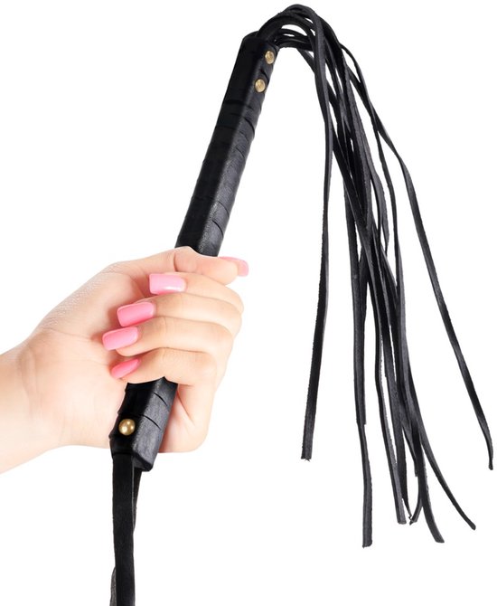 Hand met roze gelakte nagels houdt een zwarte leren zweep vast met een geribbeld handvat en dunne leren stroken.