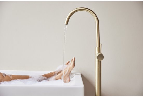 Benen van een persoon in een ligbad met schuim. Een gouden kraan sproeit water in het bad.