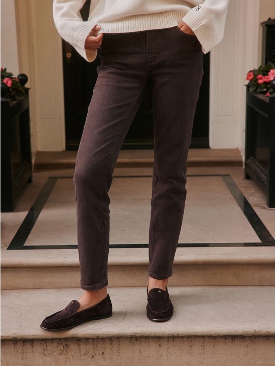 Model draagt een bruine slim-fit jeans en donkere instappers op een trap.