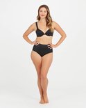 Model draagt een zwarte bh en bijpassende zwarte corrigerende slip met hoge taille, hand in de zij.