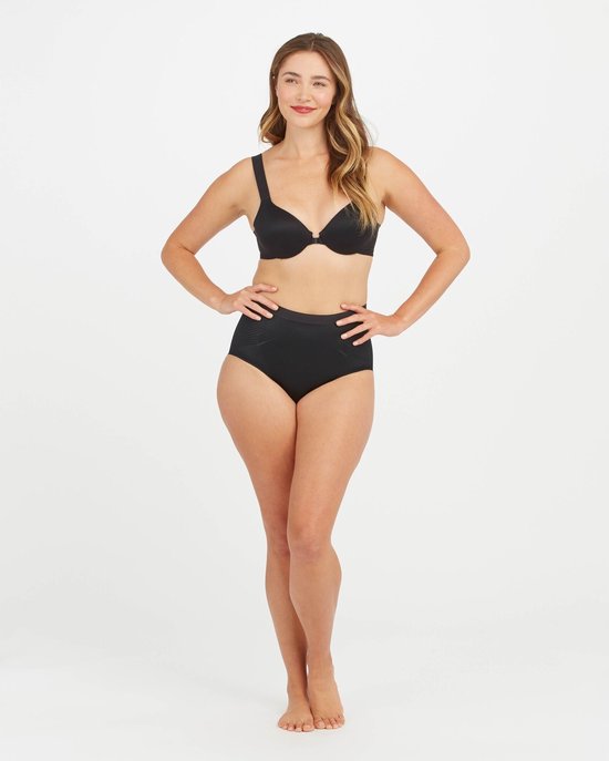 Model draagt een zwarte bh en bijpassende zwarte corrigerende slip met hoge taille, hand in de zij.