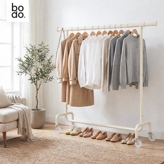 Crème kledingrek met kleding en schoenen in een sfeervol interieur met een plant en fauteuil.
