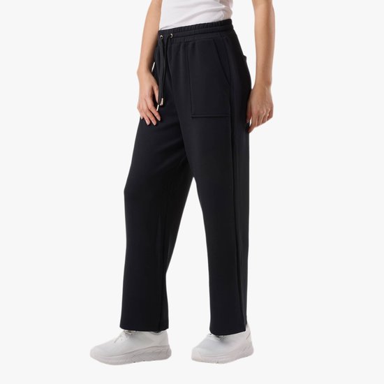 Model draagt een zwarte broek met wijde pijpen, hoge taille, koord en zakken, gecombineerd met witte sneakers.