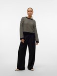 Model draagt een zwart-witte gestreepte trui met lange mouwen en zwarte broek met wijde pijpen.