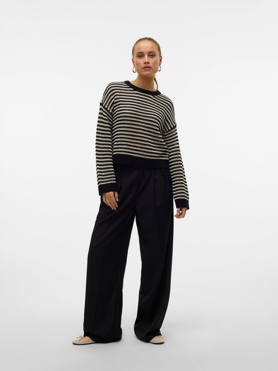 Model draagt een zwart-witte gestreepte trui met lange mouwen en zwarte broek met wijde pijpen.
