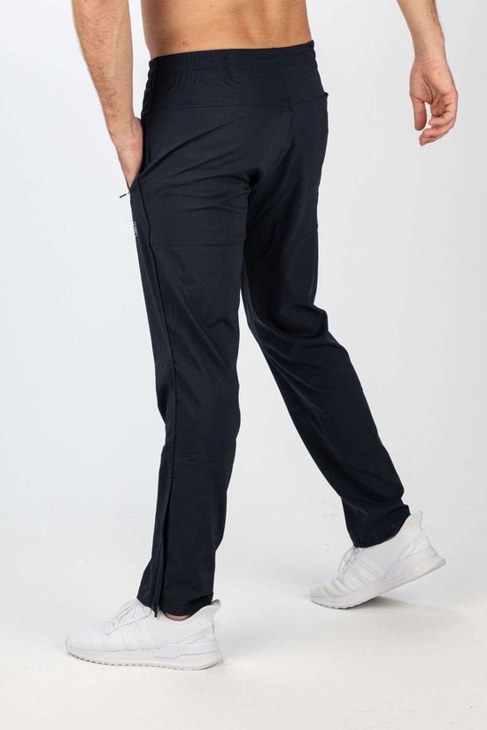 Donkerblauwe sportbroek van Sjeng Sports met ritsen aan de zijkant, gedragen door een man met witte schoenen.