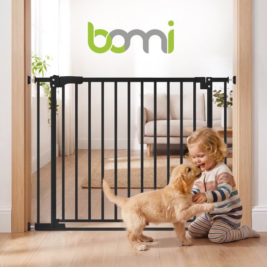 Zwart Bomi traphekje in een deuropening, met een peuter die met een puppy speelt in een woonkamer.