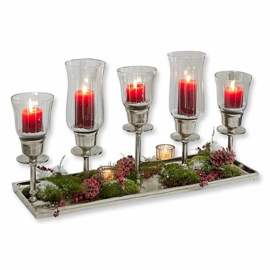 Zilverkleurige kandelaar met vijf rode kaarsen in glazen windlichten, versierd met mos en rode bessen.