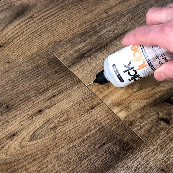 Hand brengt Madison Clark Click Lube aan tussen houten vloerdelen met een klikverbinding.