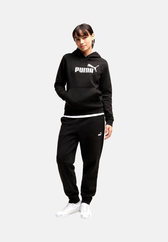 Model in een zwarte Puma hoodie en joggingbroek, handen in de zakken van de broek.