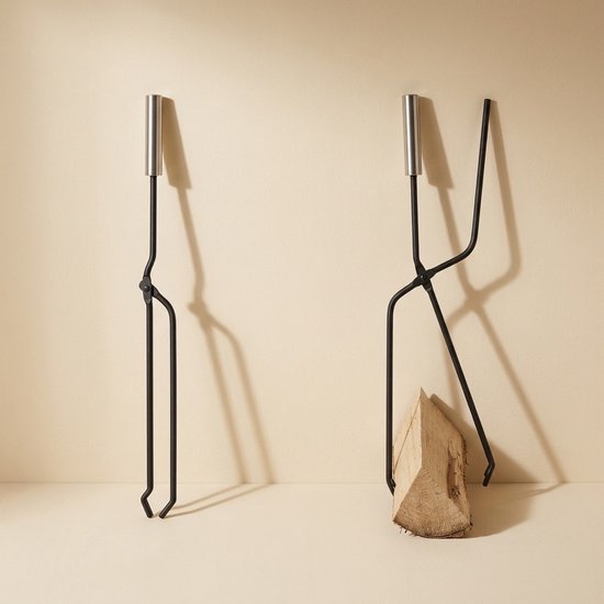 Zwarte metalen haardtangen met zilverkleurige handvatten, een met een stuk brandhout.
