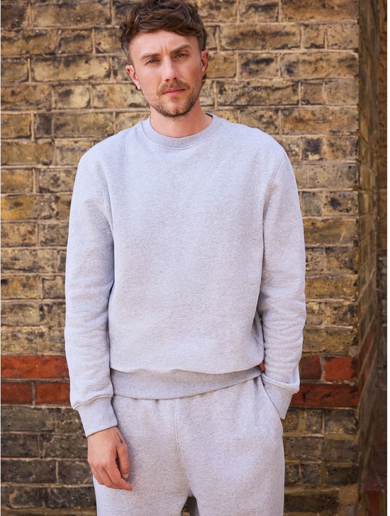 Model draagt een grijs sweatshirt met ronde hals en bijpassende joggingbroek, handen in de zakken.