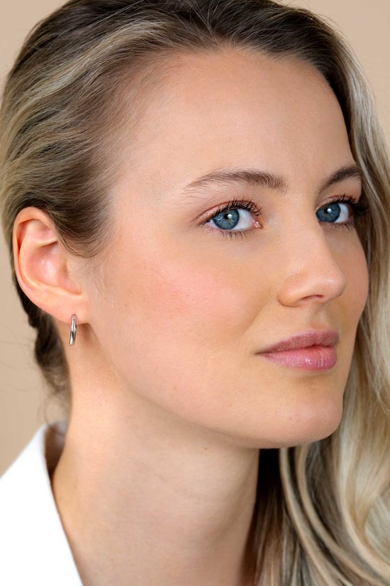 Model draagt een zilveren oorringetje met een gladde afwerking.