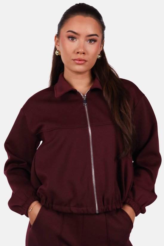 Close-up van model in een bordeauxrood vest met opstaande kraag en zilveren rits.
