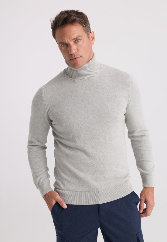 Model draagt een grijze coltrui met geribbelde boorden, gecombineerd met een donkerblauwe broek.