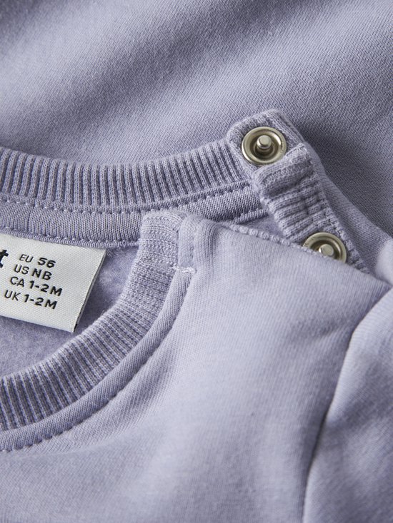 Detail van de schouder van een lichtpaarse sweater met drukknoopsluiting en maatlabel EU 56.