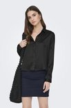Model draagt zwarte satijnen blouse met knoopjes, een donkerblauwe rok en zwarte laarzen.