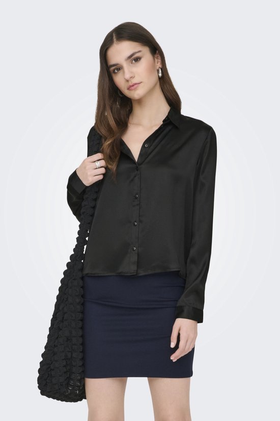 Model draagt zwarte satijnen blouse met knoopjes, een donkerblauwe rok en zwarte laarzen.