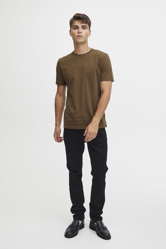 Man in een olijfbruin gemêleerd T-shirt, zwarte broek en zwarte loafers.